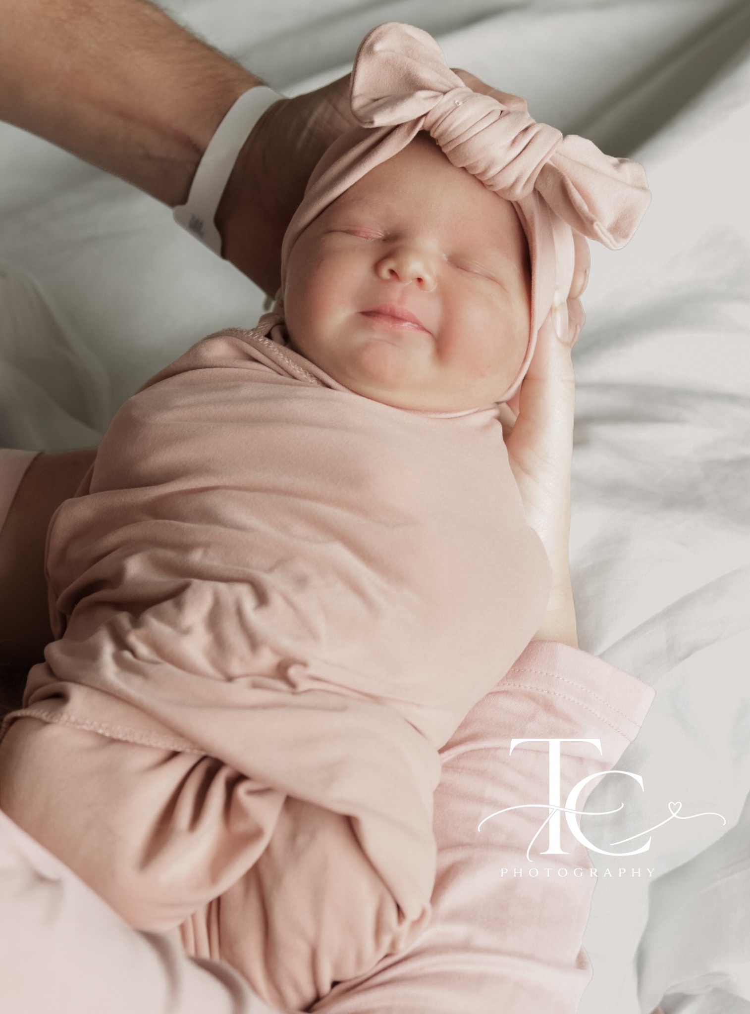 Newborn in a pink swaddle and bow held in a parent’s hands