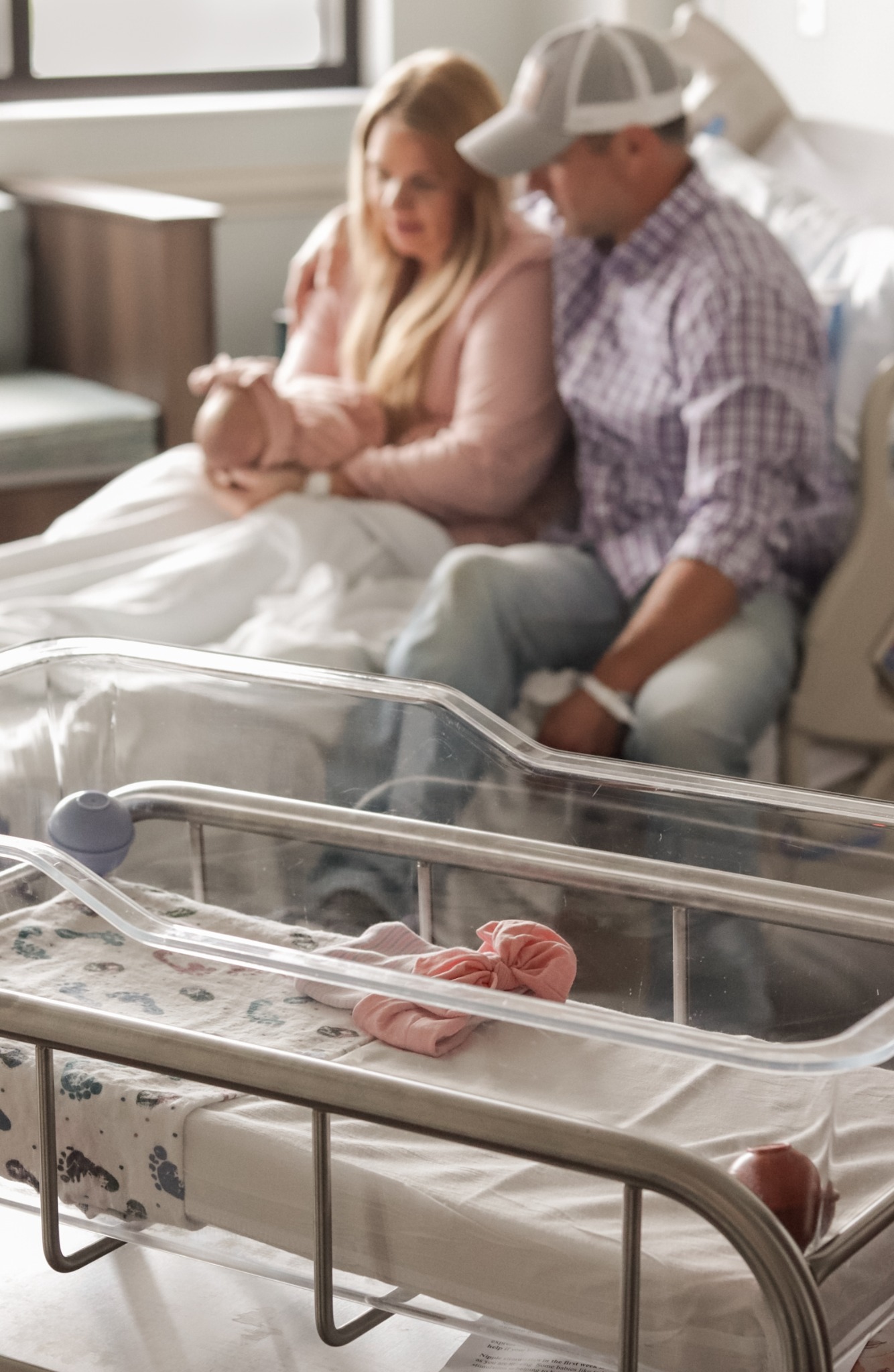 Parents seated together holding their newborn beside a hospital bassinet