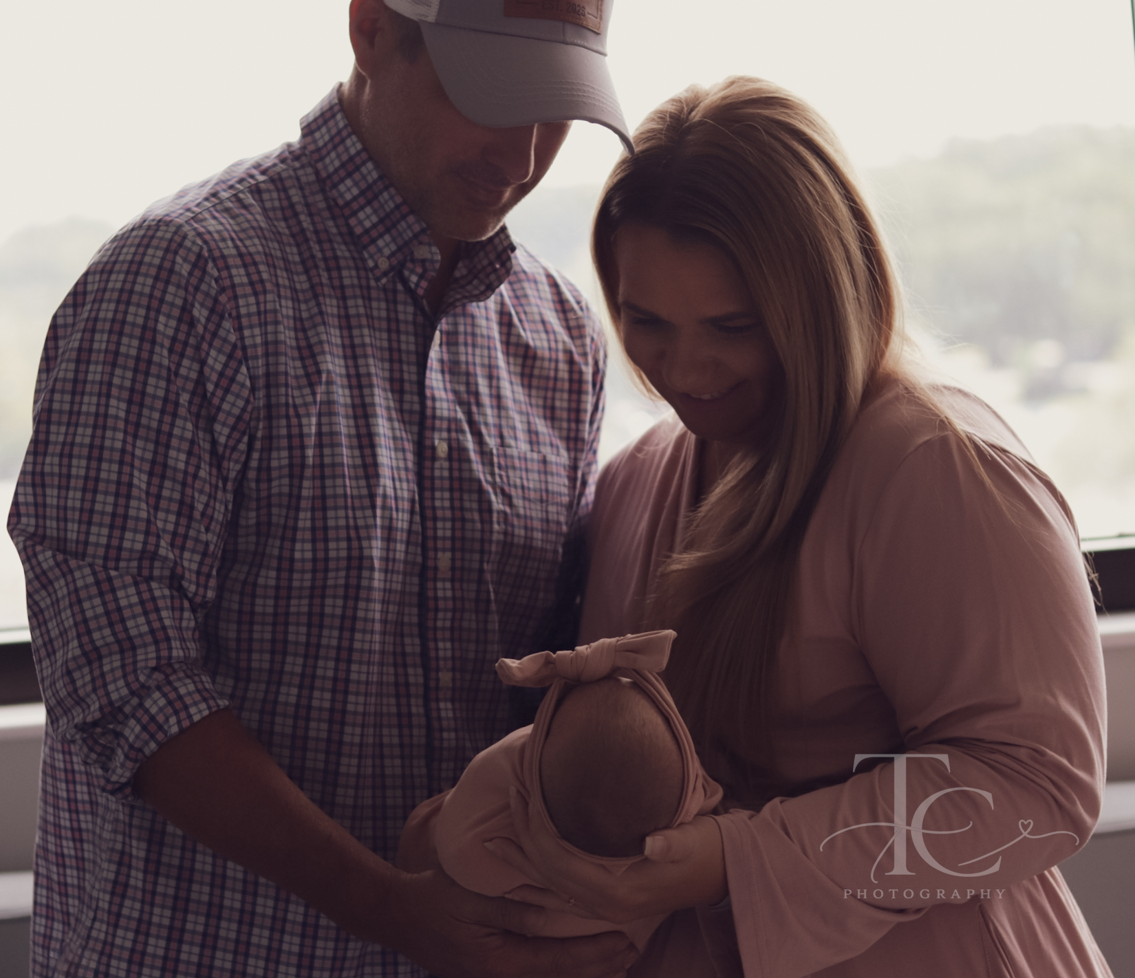 Parents standing by a window and cuddling their newborn