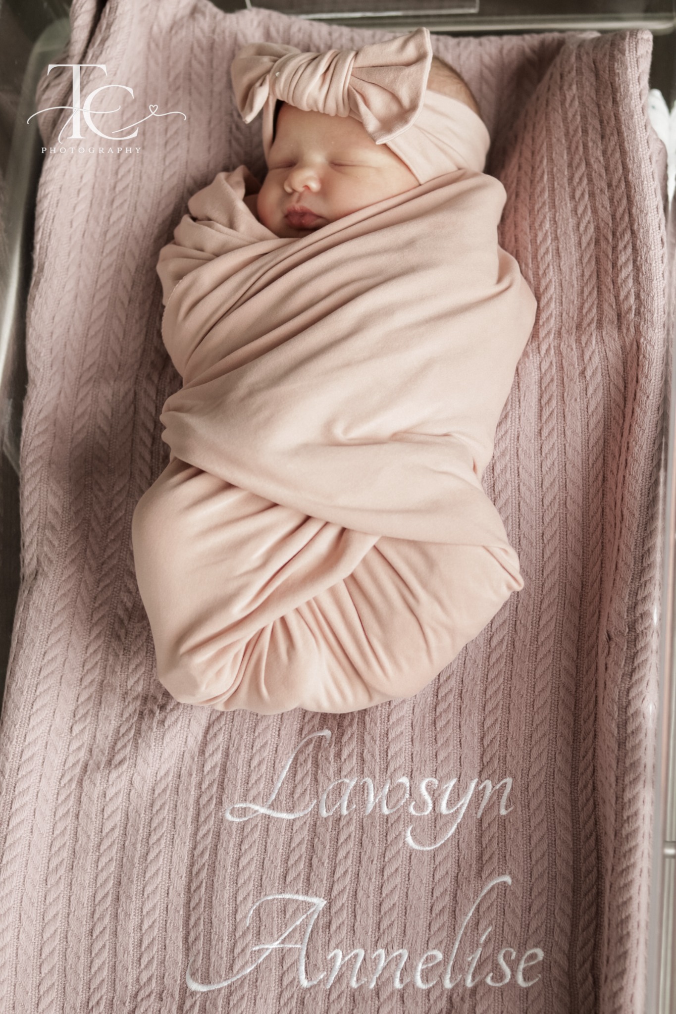 Newborn sleeping in a pink wrap on a personalized blanket