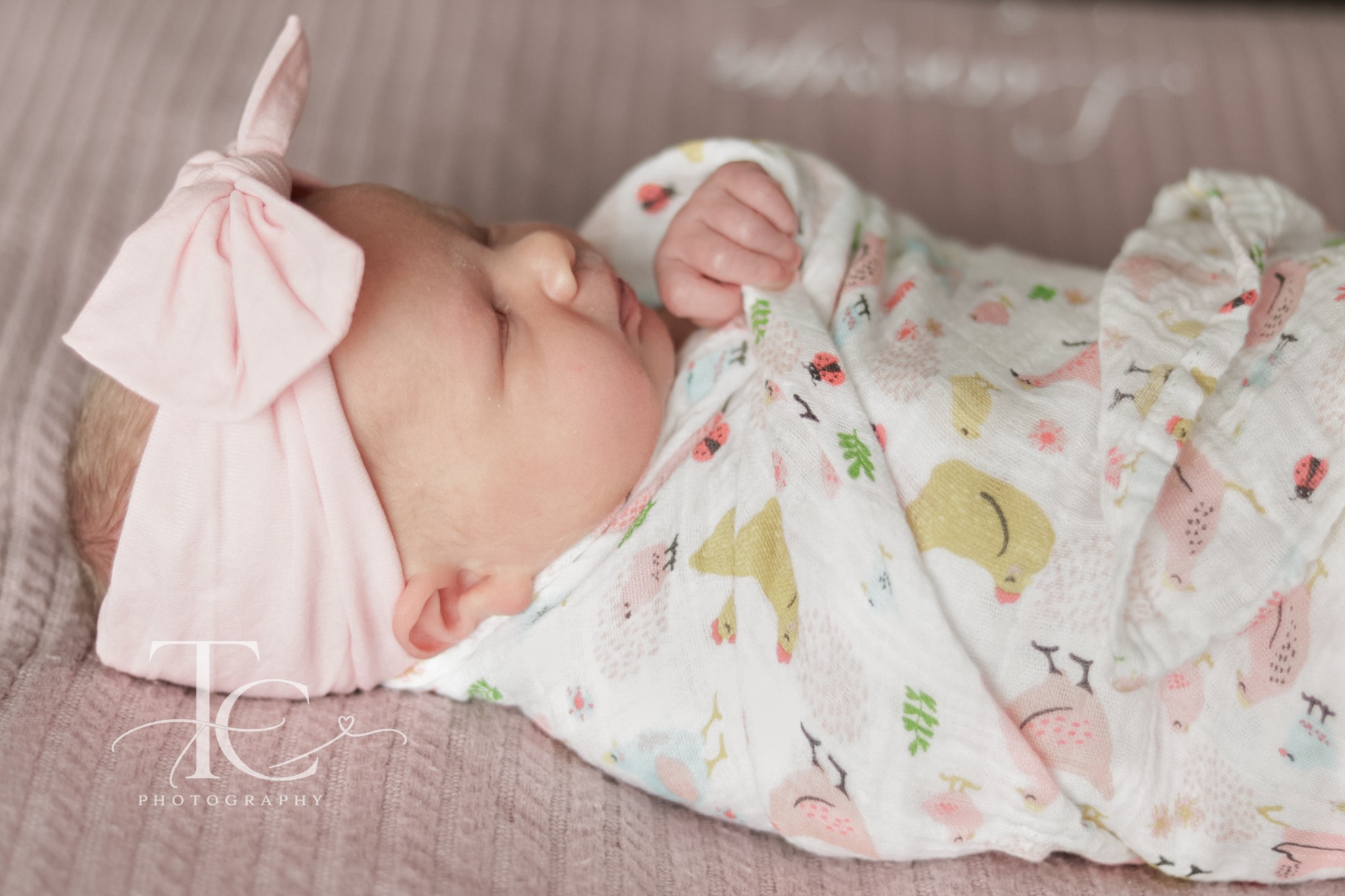 Newborn sleeping in a floral wrap and pink bow