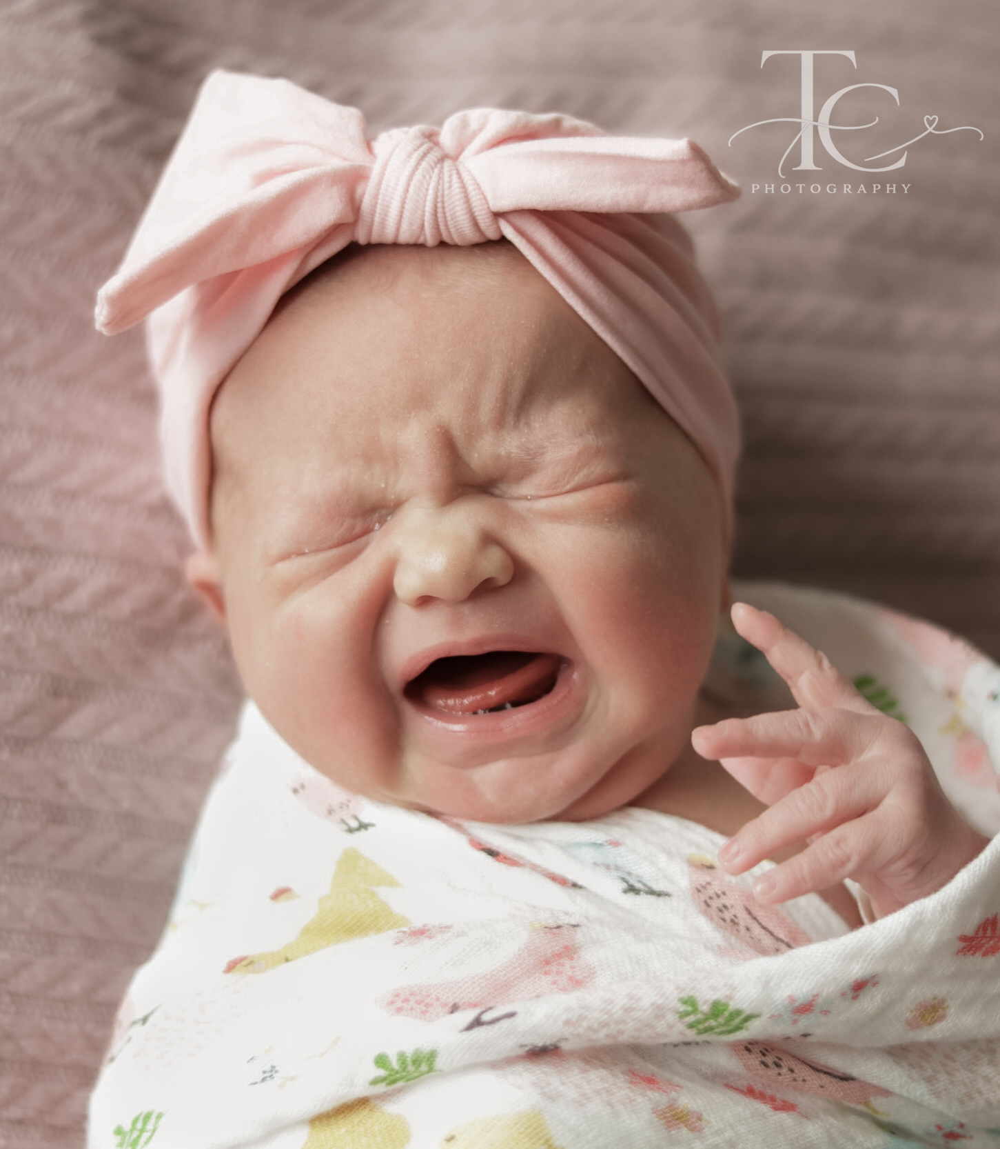 Newborn with a pink bow stretching and crying