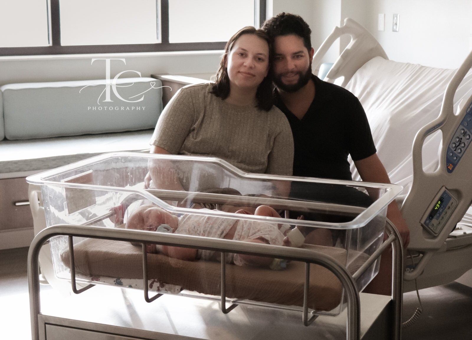Parents seated behind their newborn’s hospital bassinet