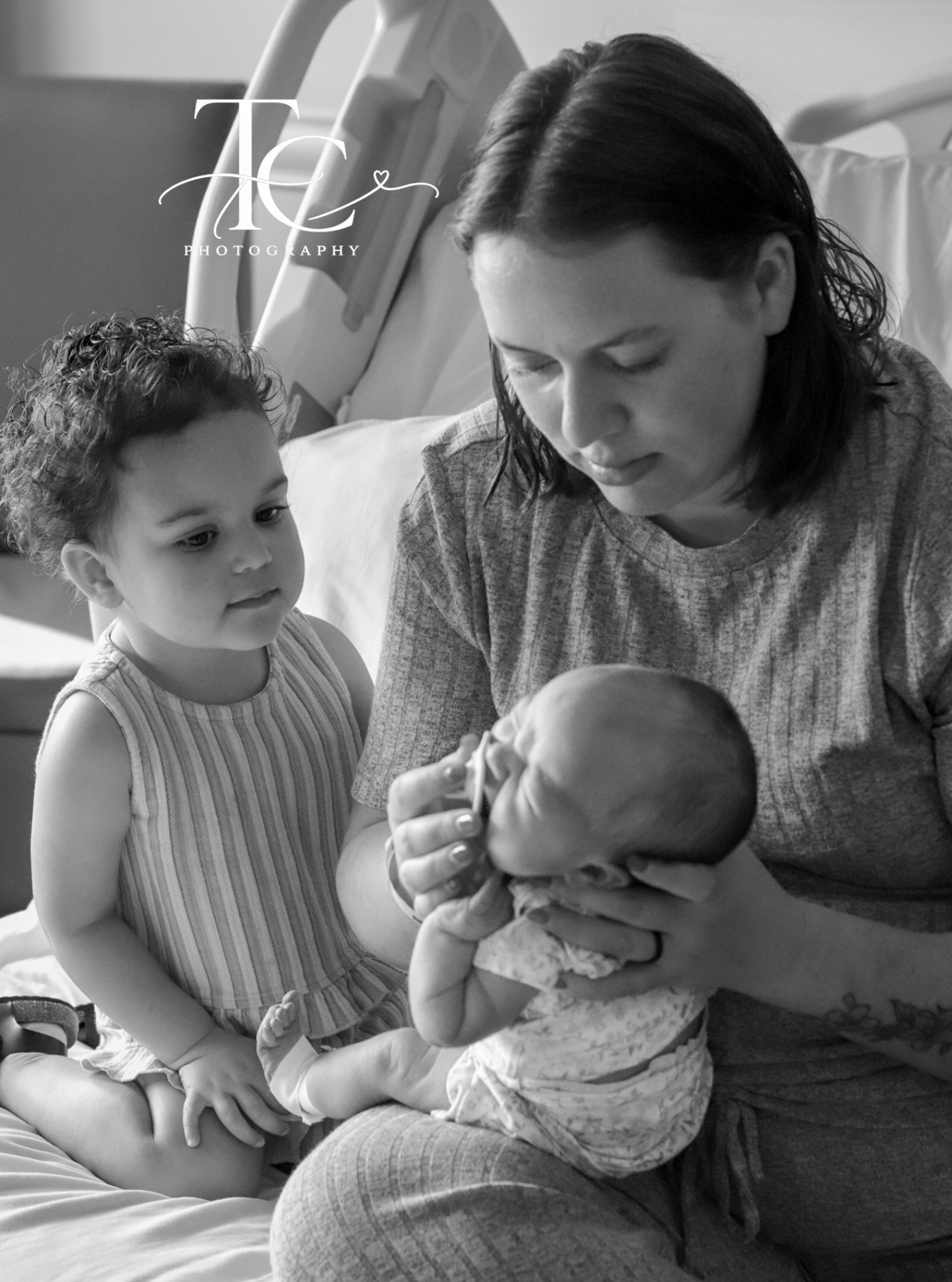 Black-and-white portrait of mother and older sibling admiring newborn