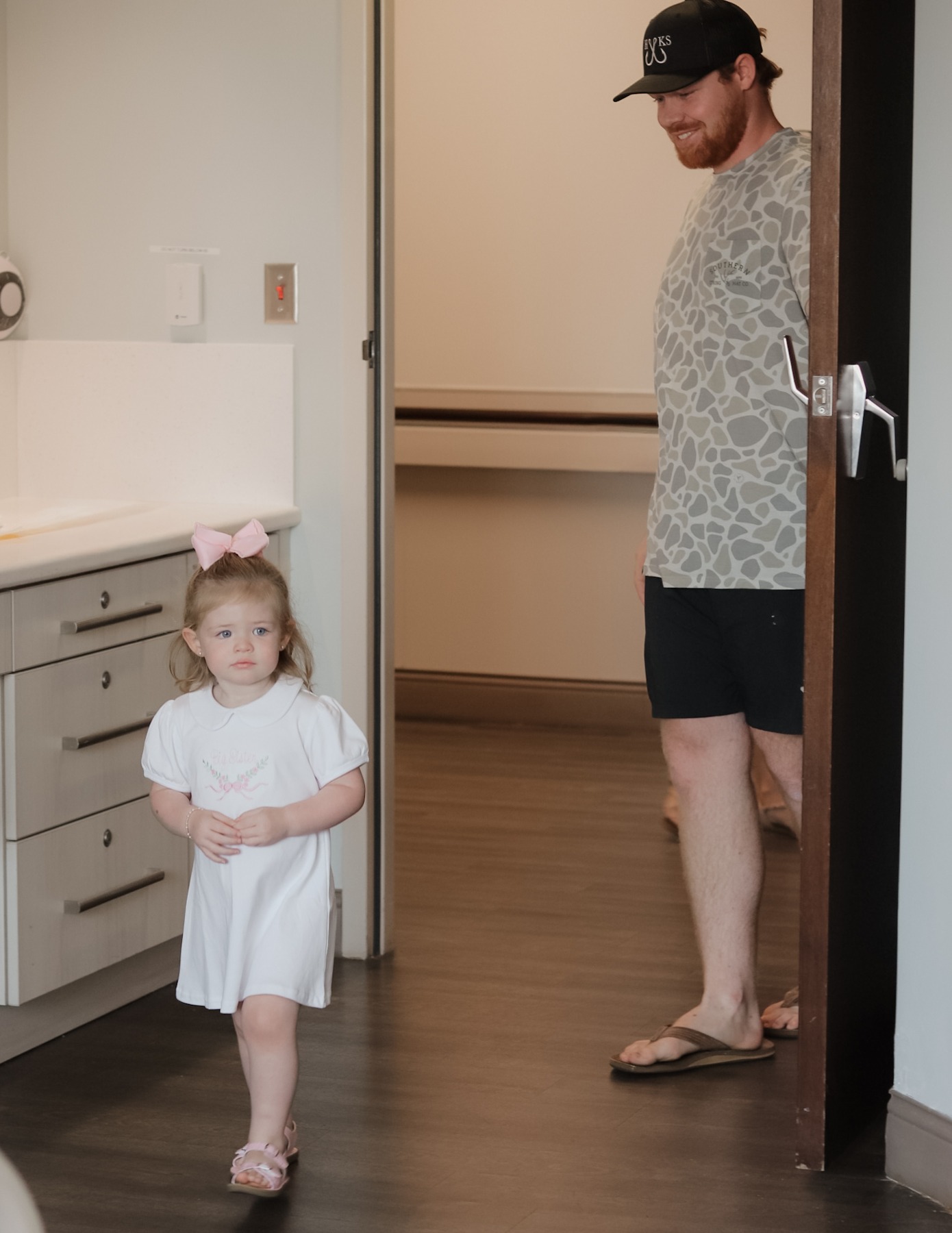 Father and young daughter entering a hospital room