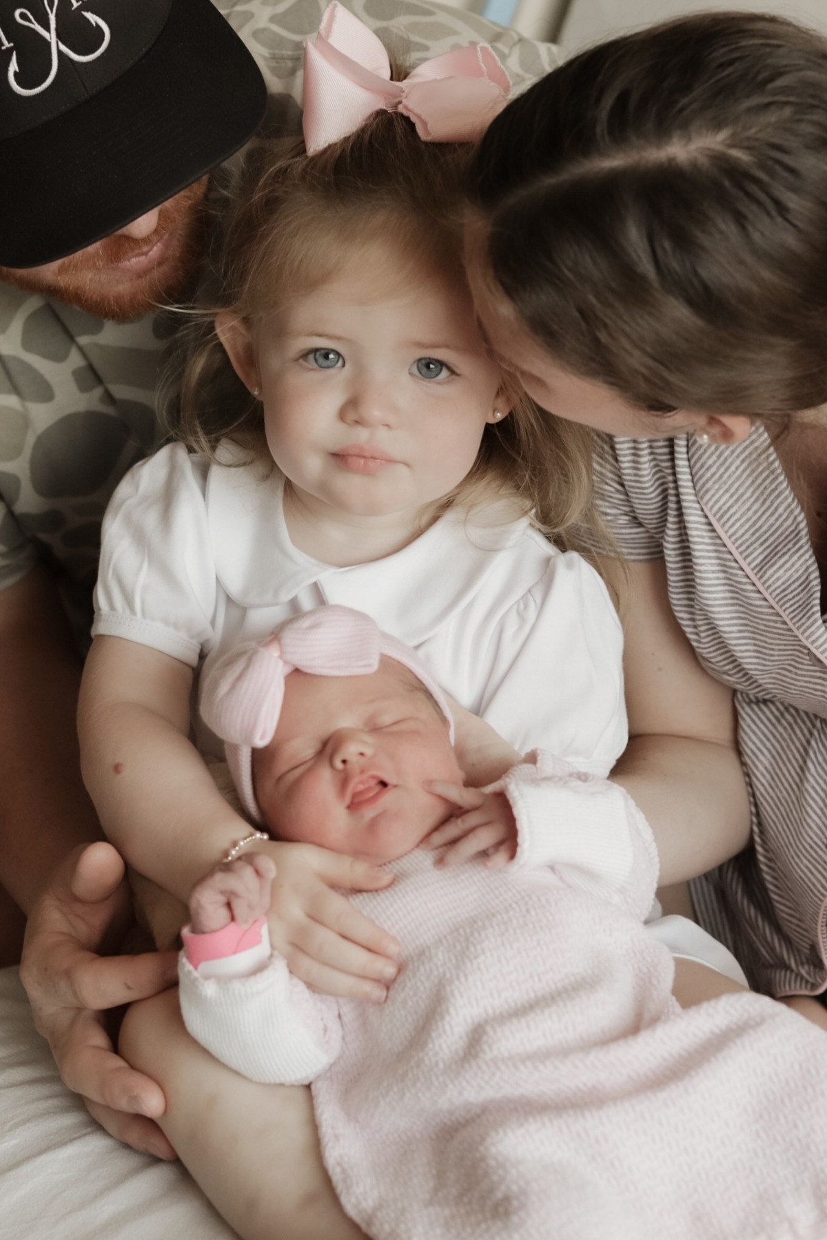 Parents kissing their older daughter as she holds her newborn sibling