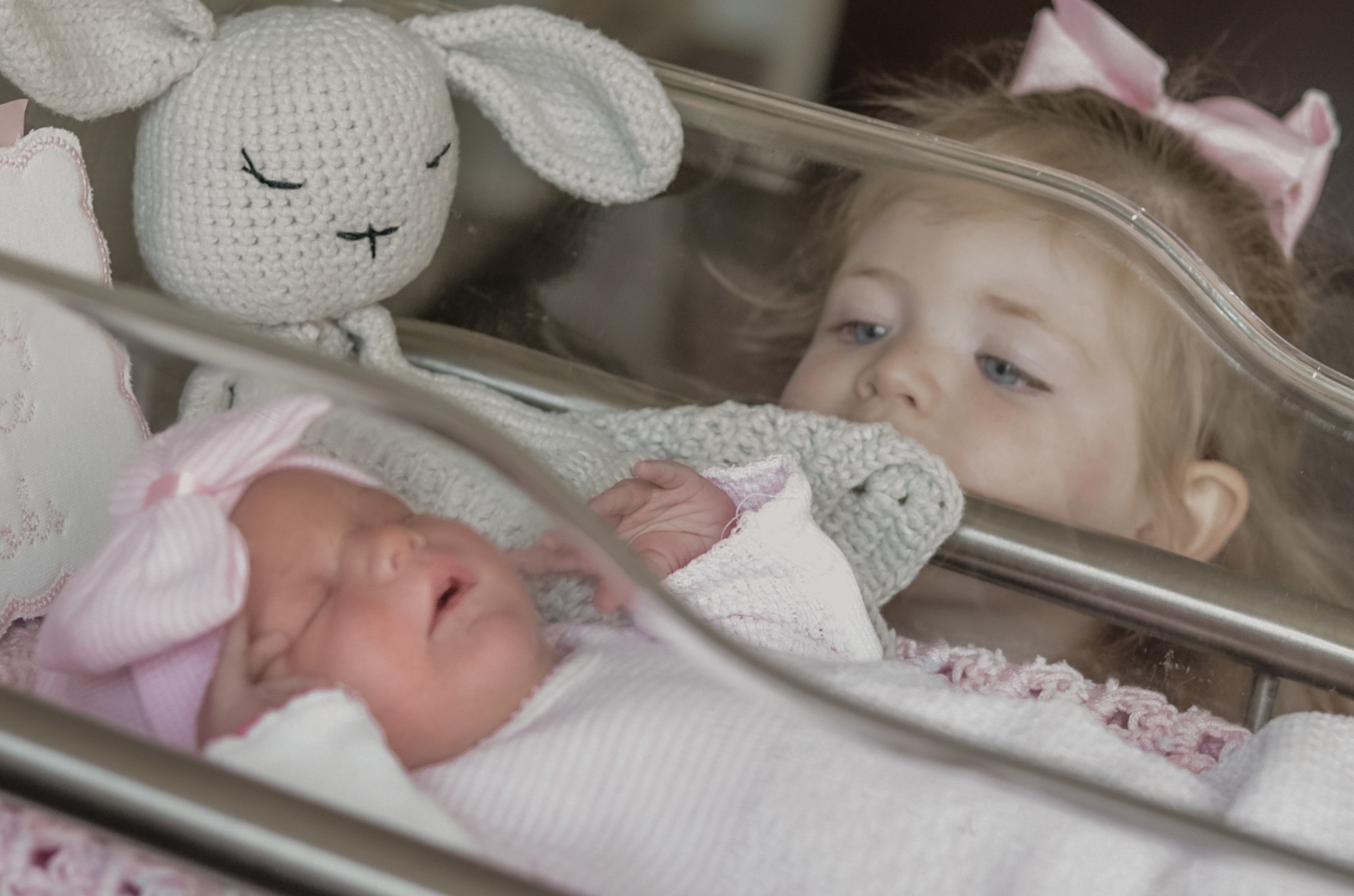 Older sister looking at her newborn sibling in a hospital bassinet