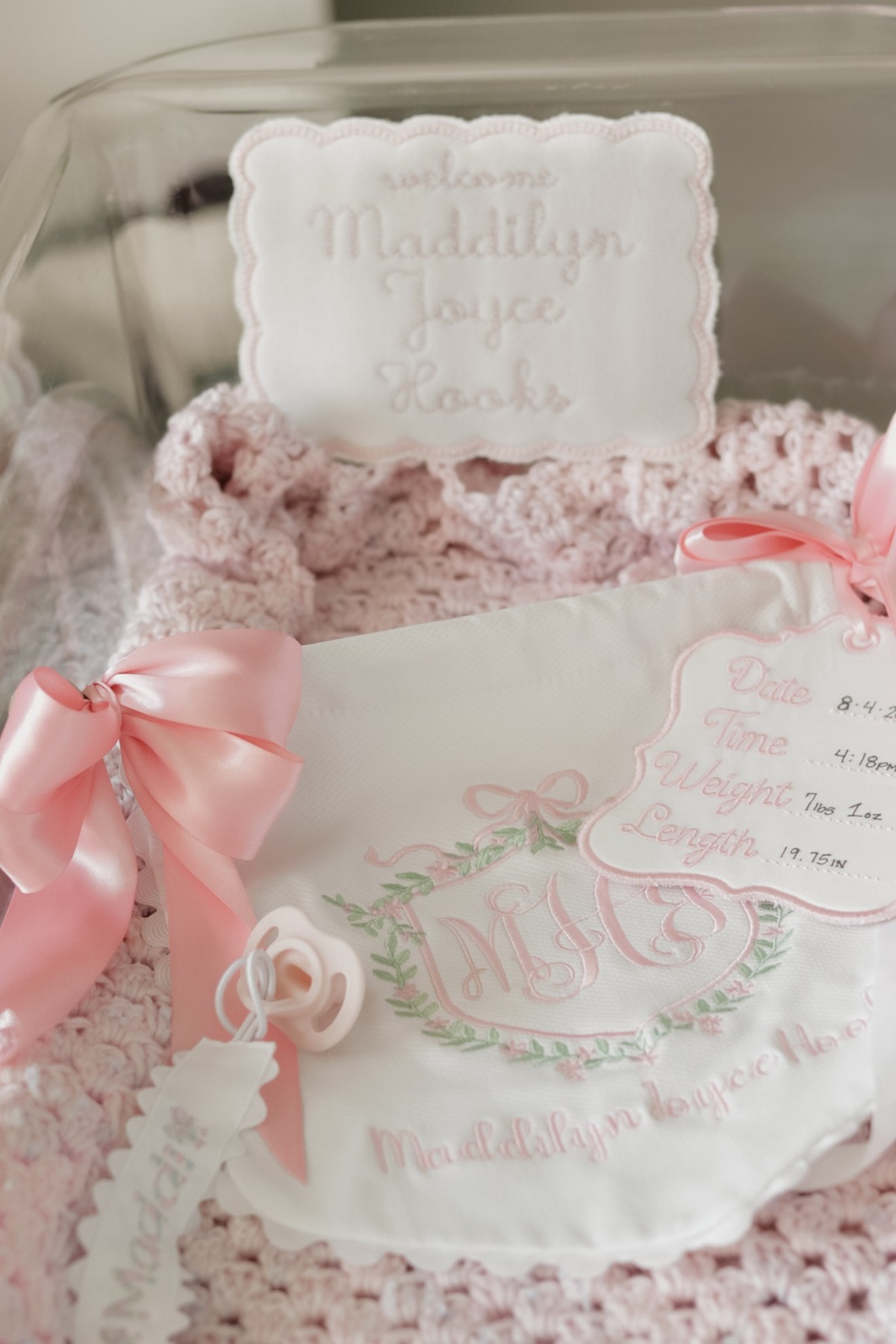 Pink newborn blanket and personalized pillow in a hospital bassinet