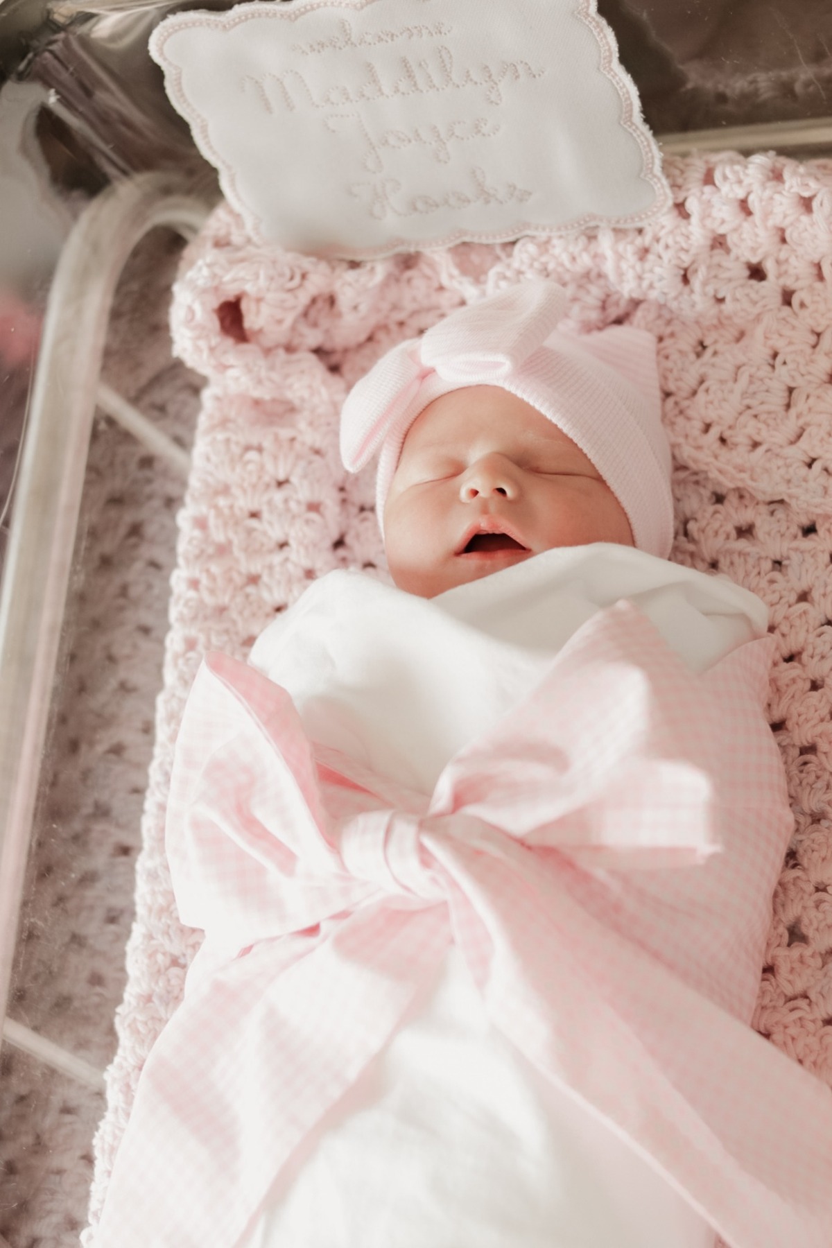 Sleeping newborn in a pink bow hat in a hospital bassinet