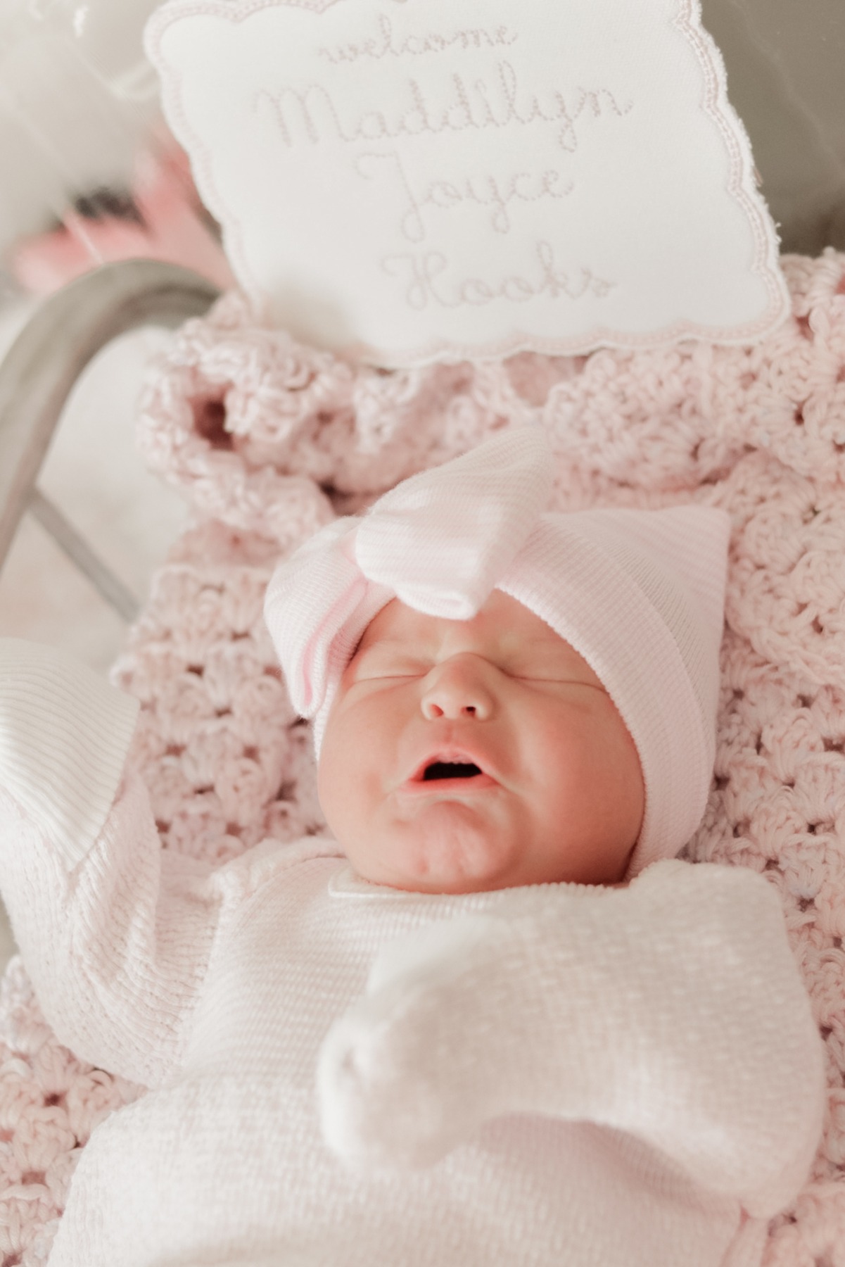 Newborn in a white swaddle beside a personalized pillow