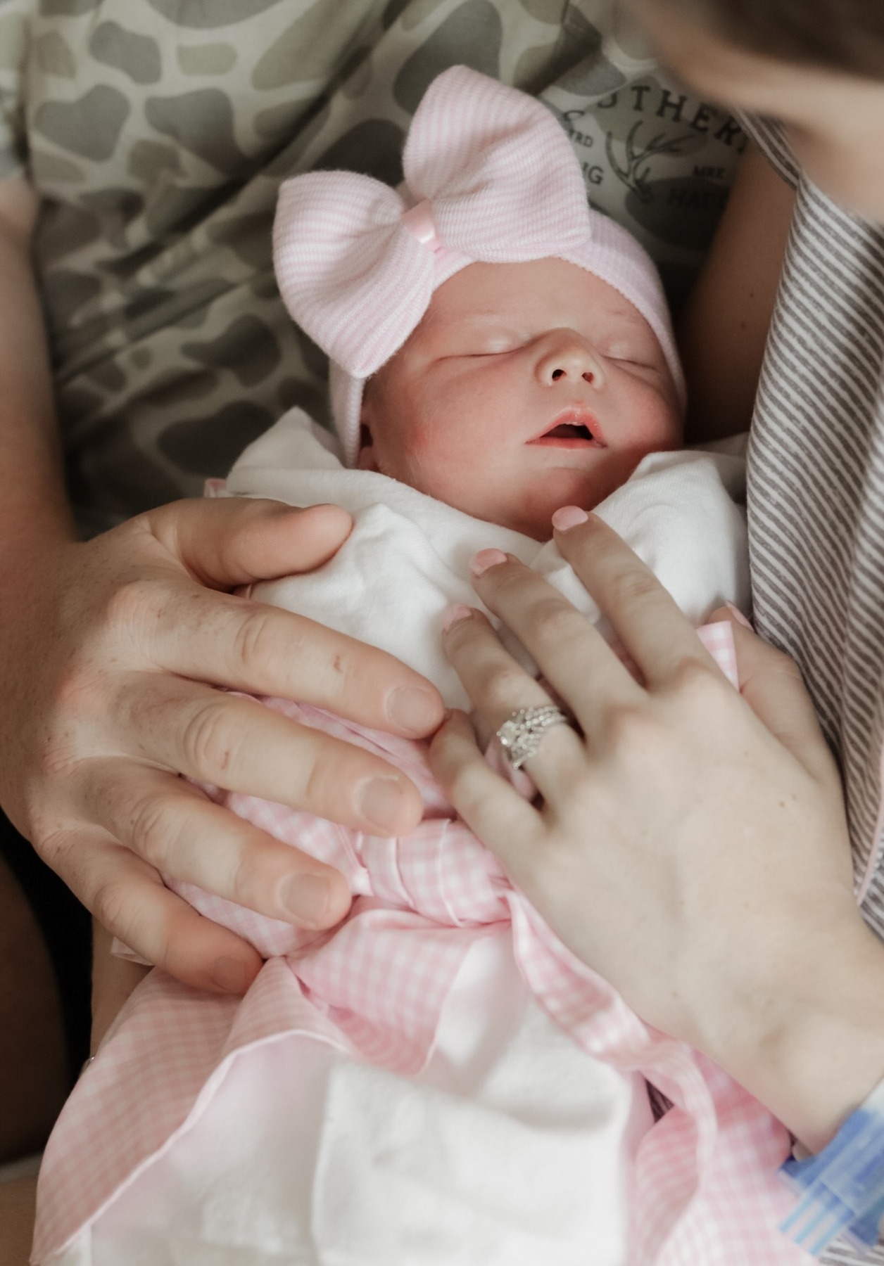 Newborn in a pink bow hat held close by a parent