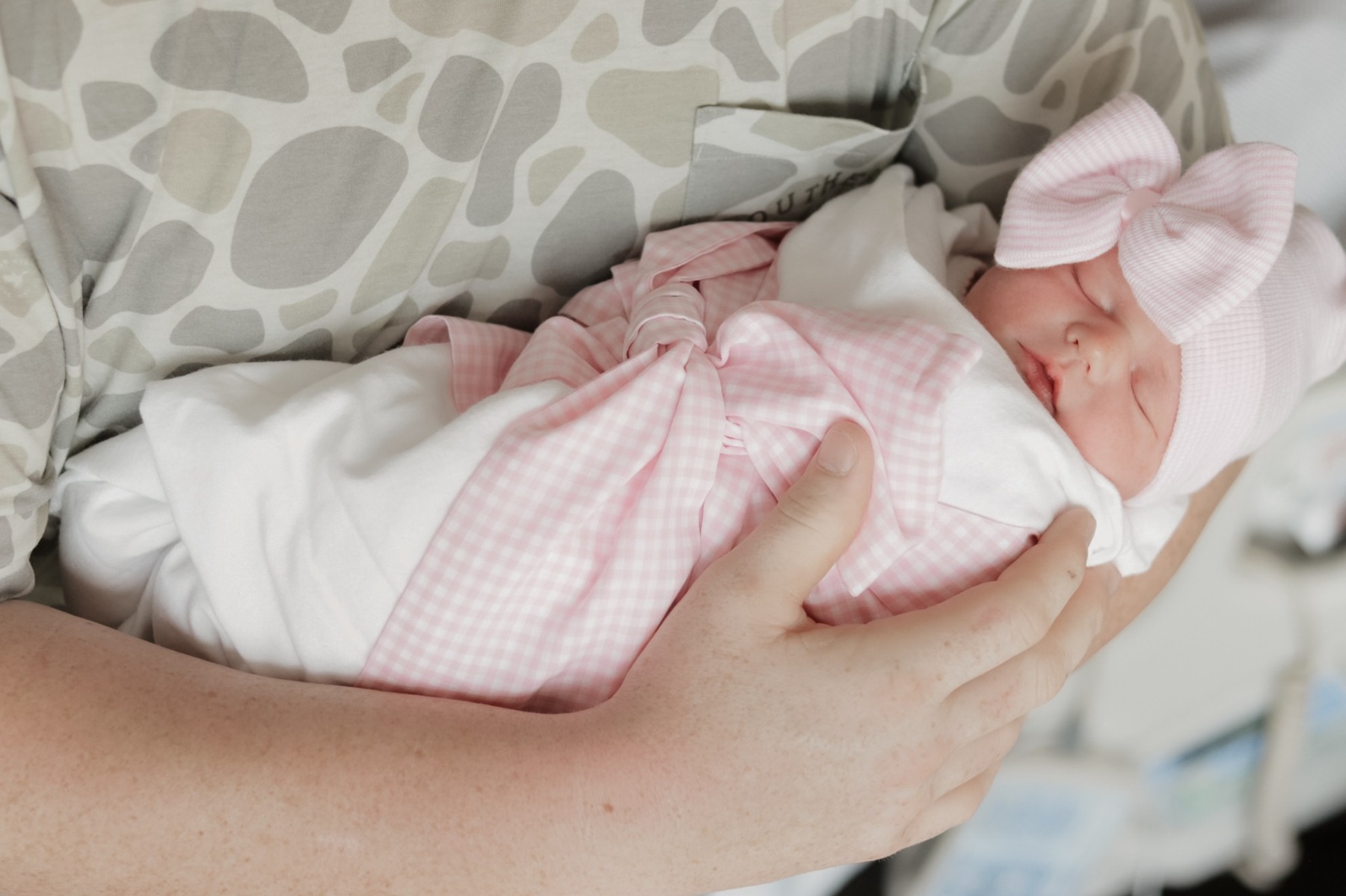 Newborn resting in a parent’s arms with a pink bow
