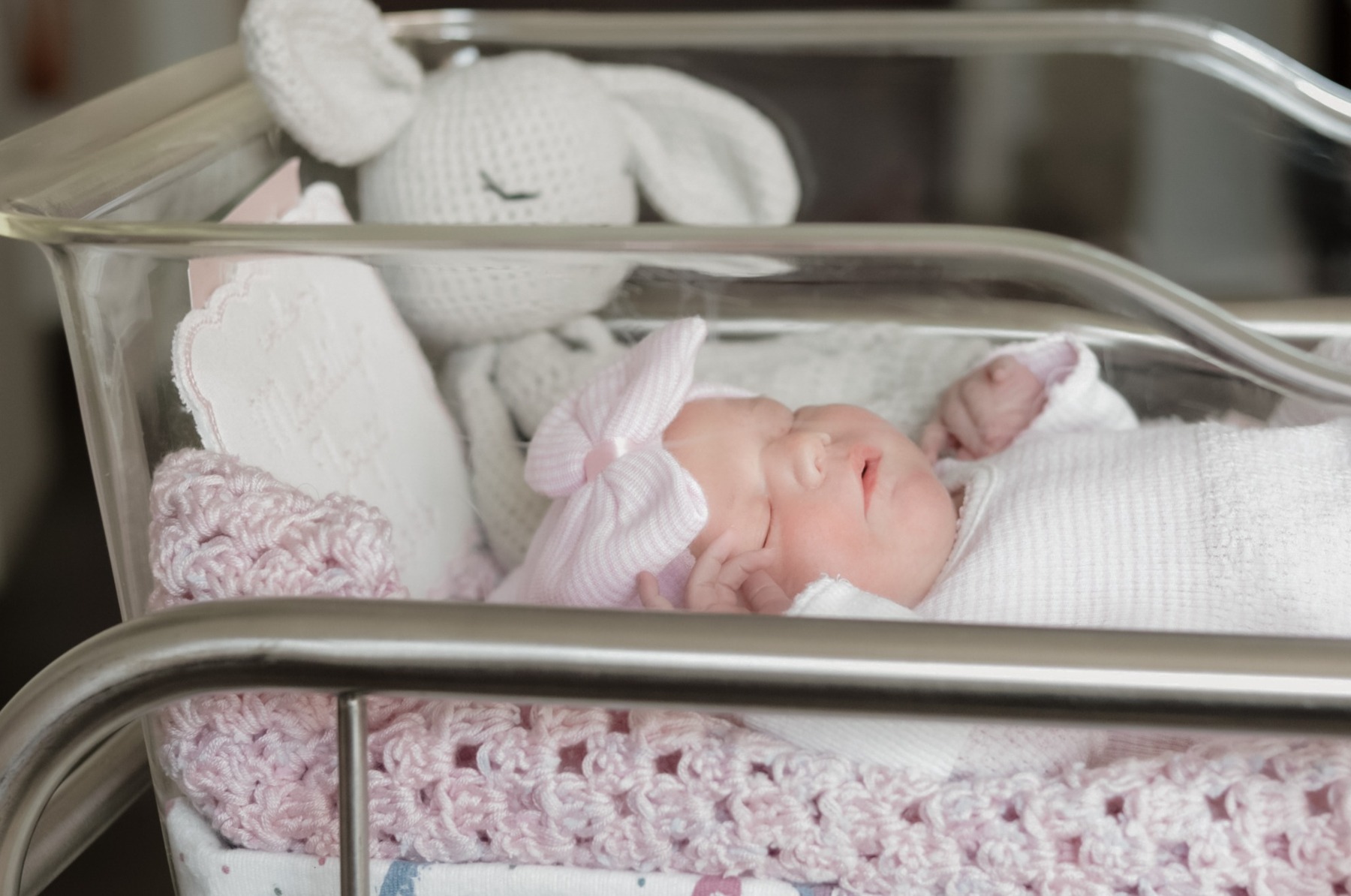 Newborn sleeping in a hospital bassinet beside a soft bunny toy
