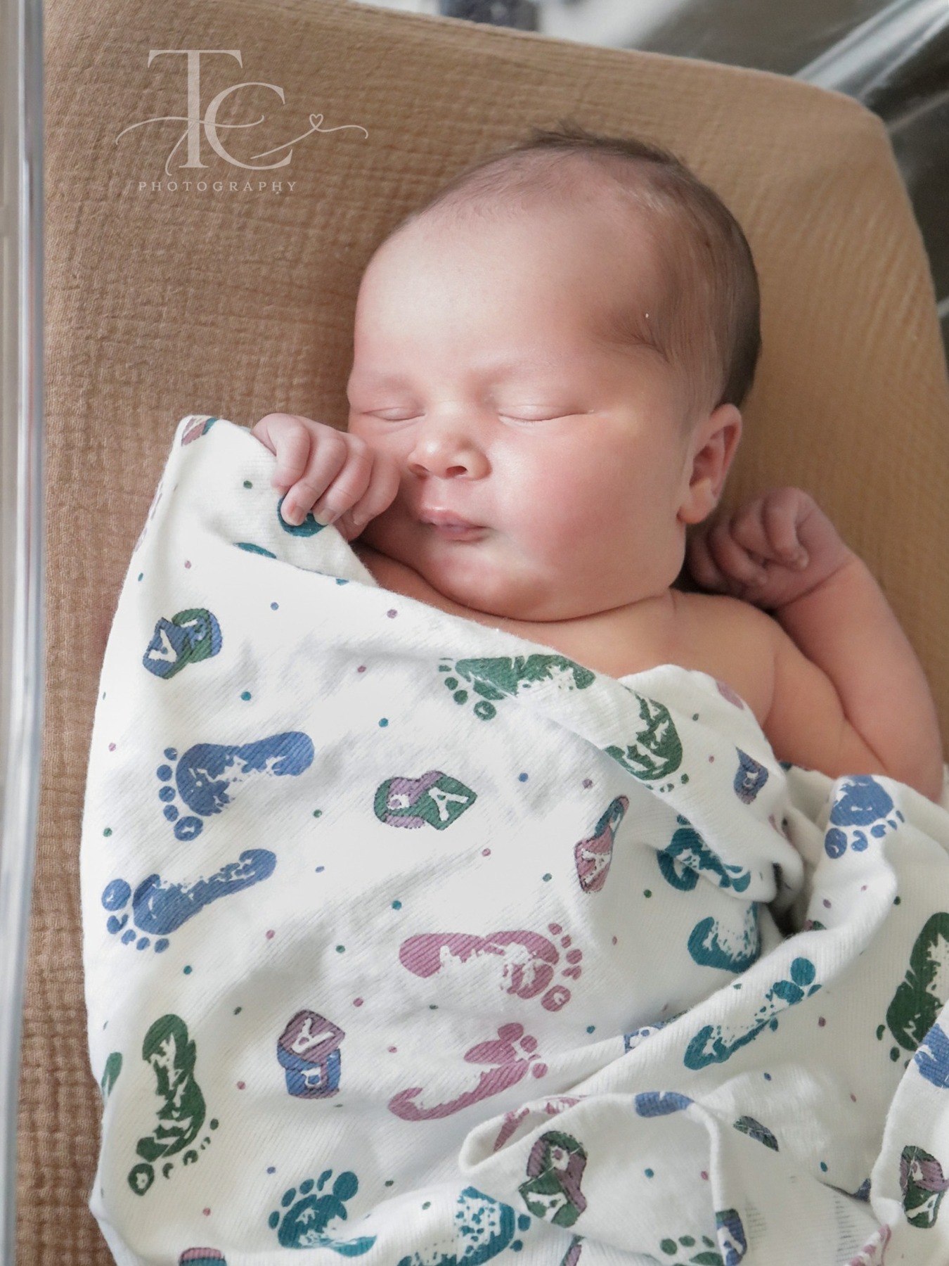 Sleeping newborn in a hospital bassinet under a footprint-patterned blanket