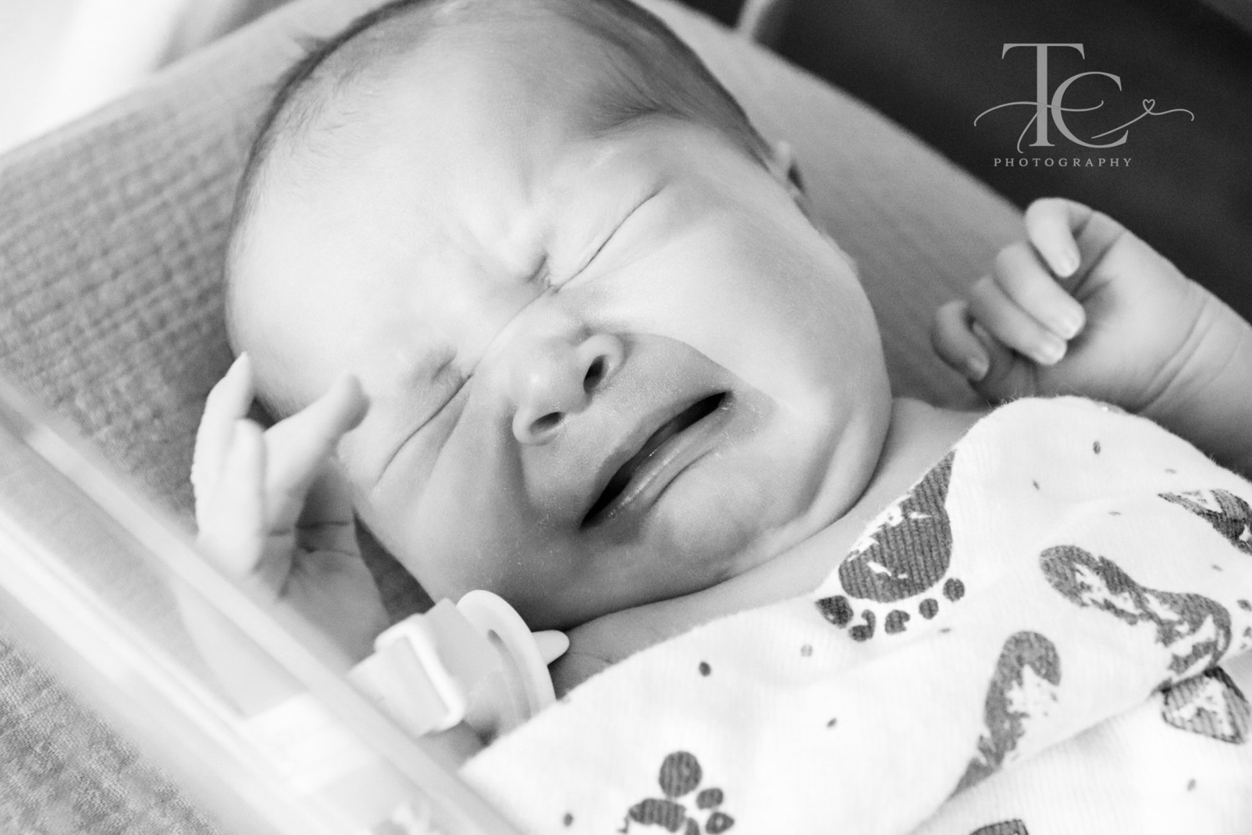 Black-and-white photograph of a newborn smiling in a hospital bassinet