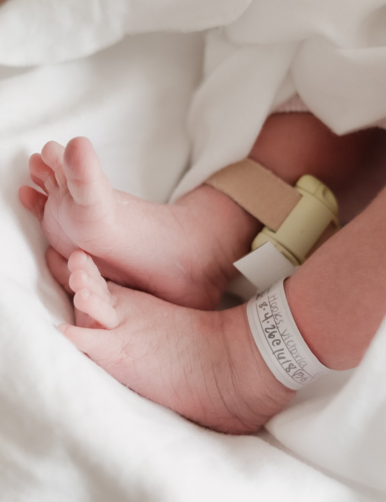 Tiny newborn feet with hospital bracelets resting on a white blanket