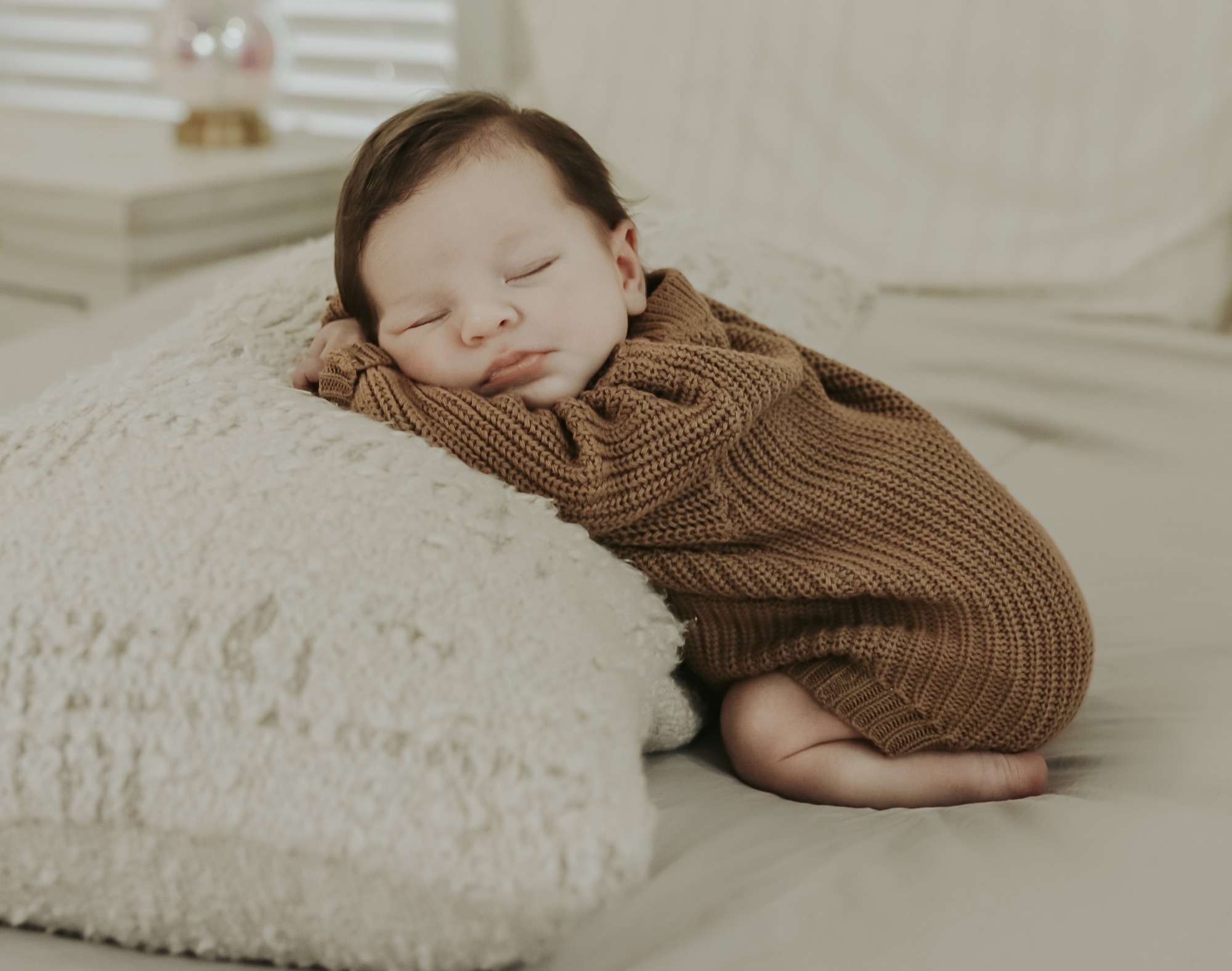 Sleeping newborn in a brown knitted outfit resting on a cream blanket