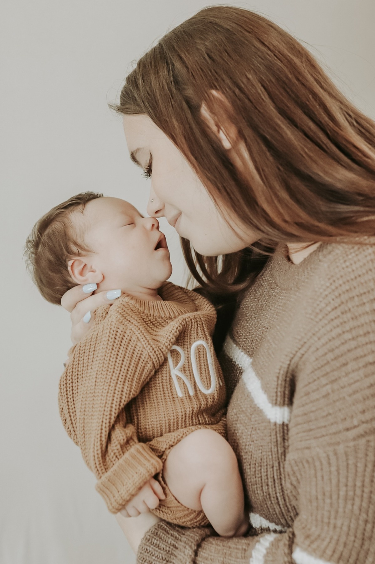 Mother gazing at her newborn in a brown knitted outfit