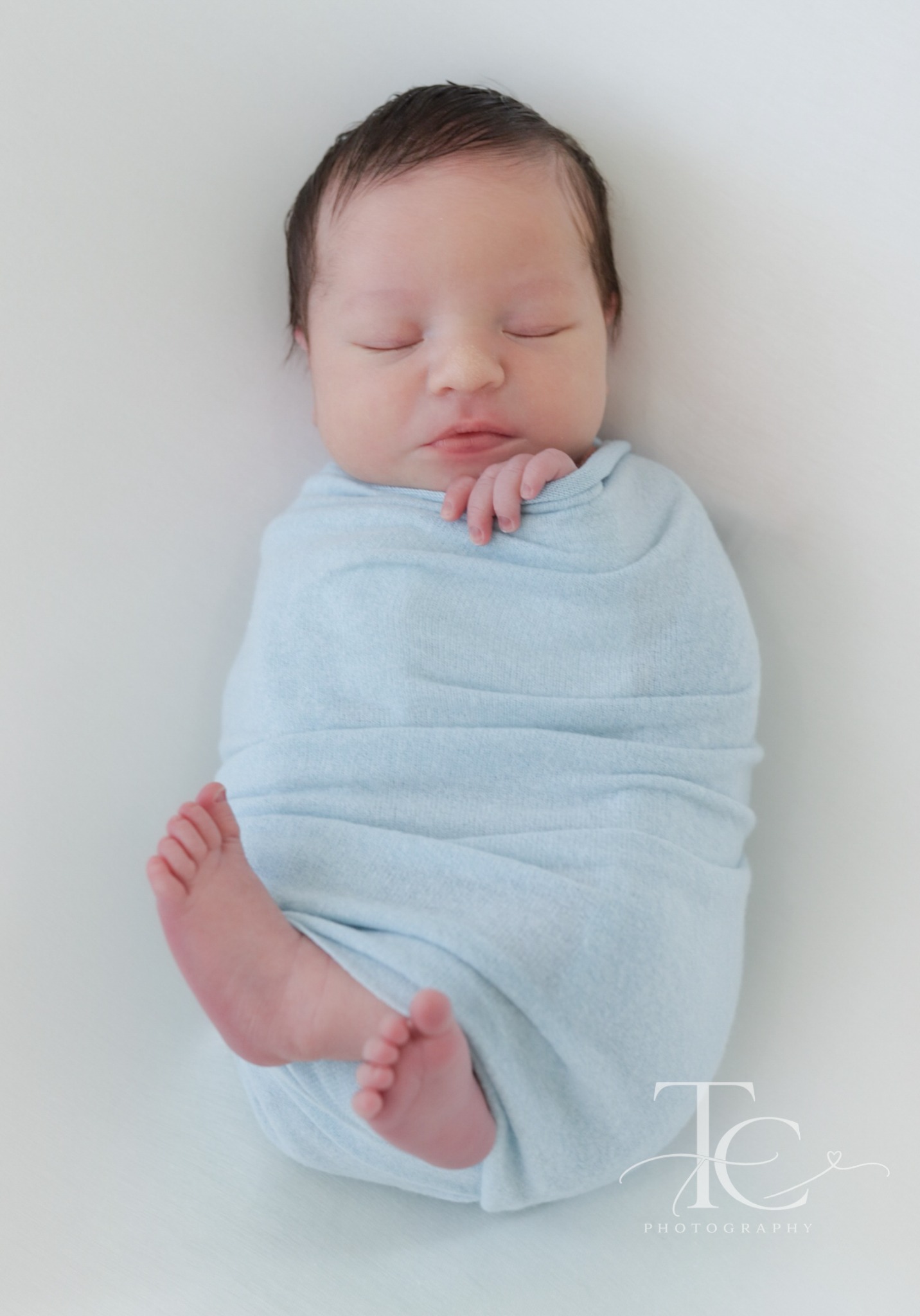 Newborn in a blue wrap with tiny feet peeking out