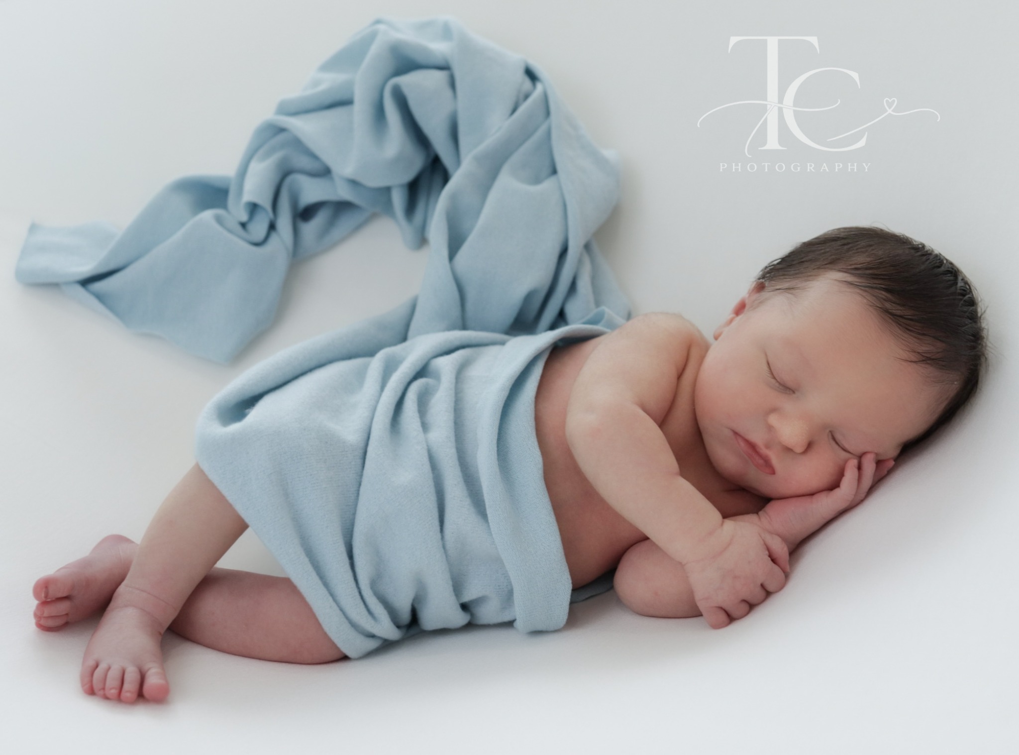 Newborn resting on a white backdrop with draped blue fabric