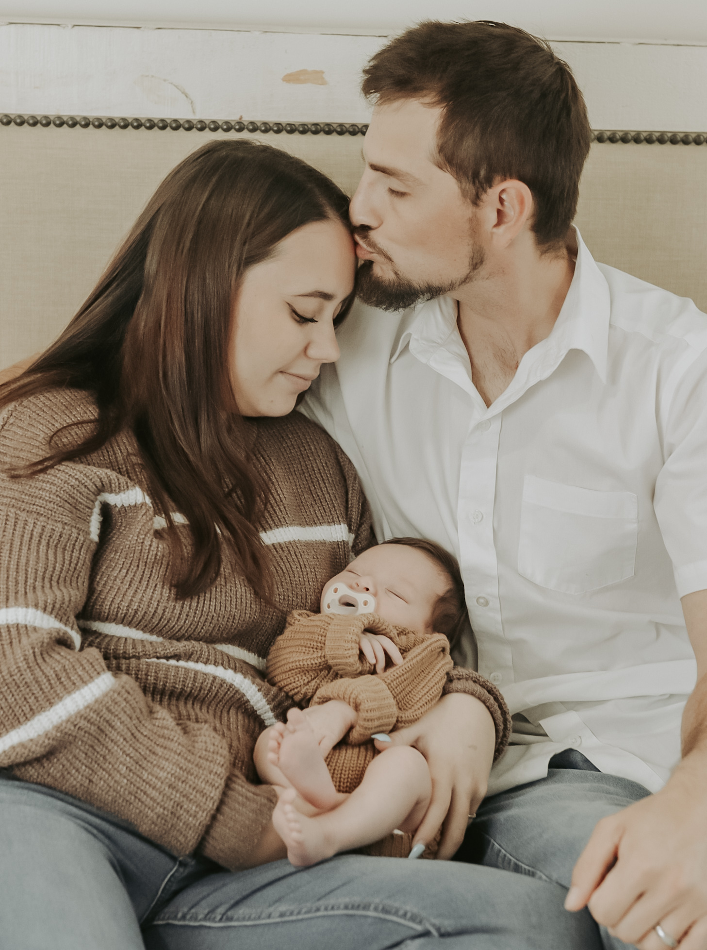 Parents lifting their newborn for a gentle kiss