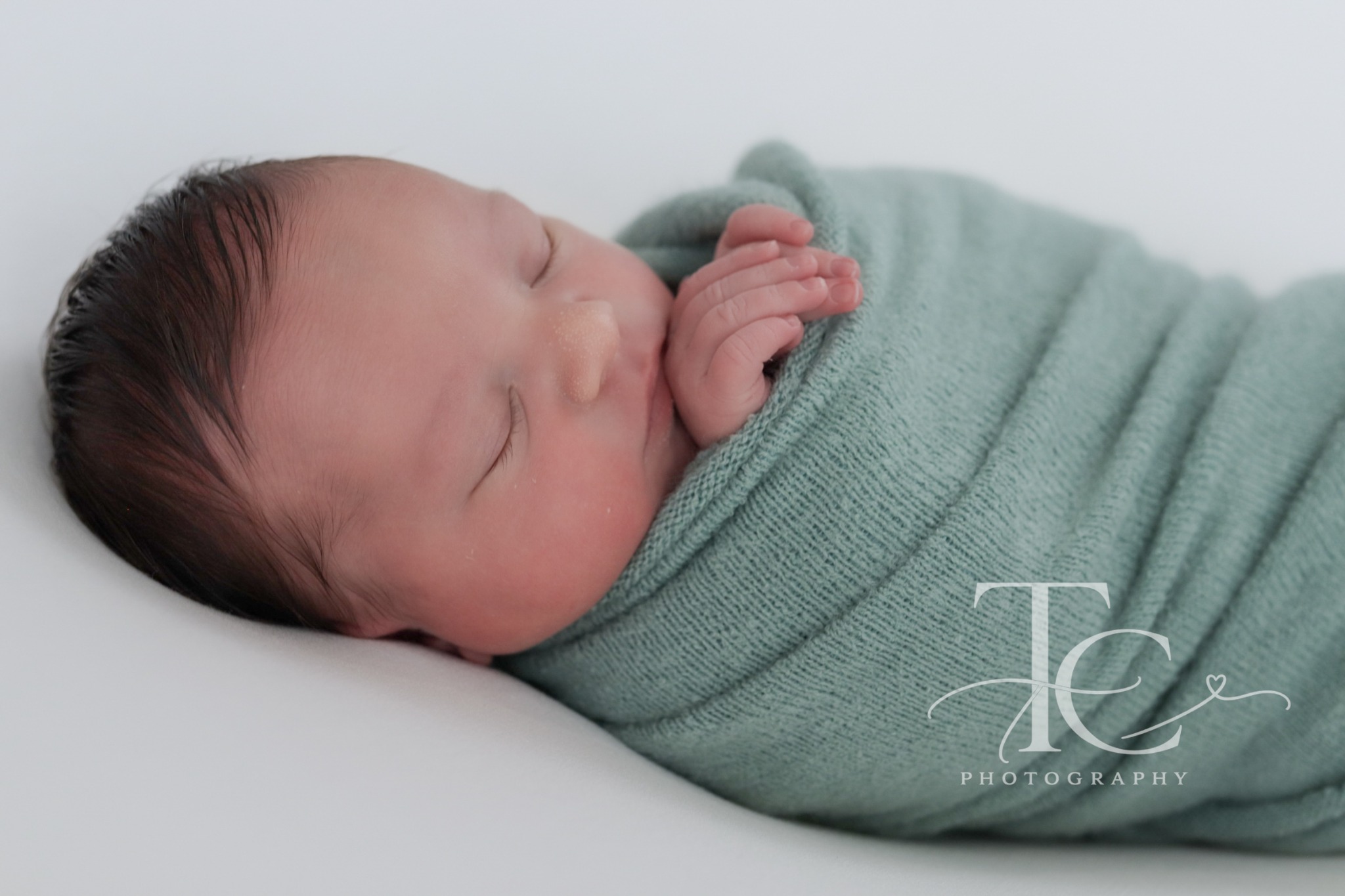 Sleeping newborn wrapped in sage green fabric