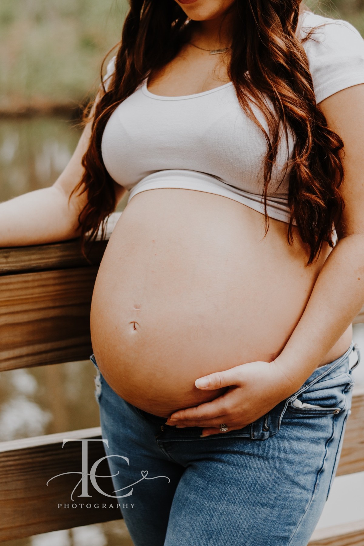 Close-up of an expectant mother holding her belly beside a wooden railing