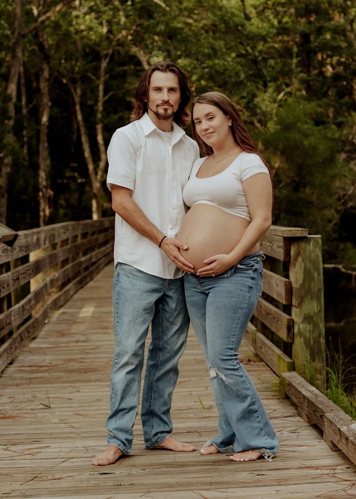 Expectant parents holding baby bump on a wooden bridge