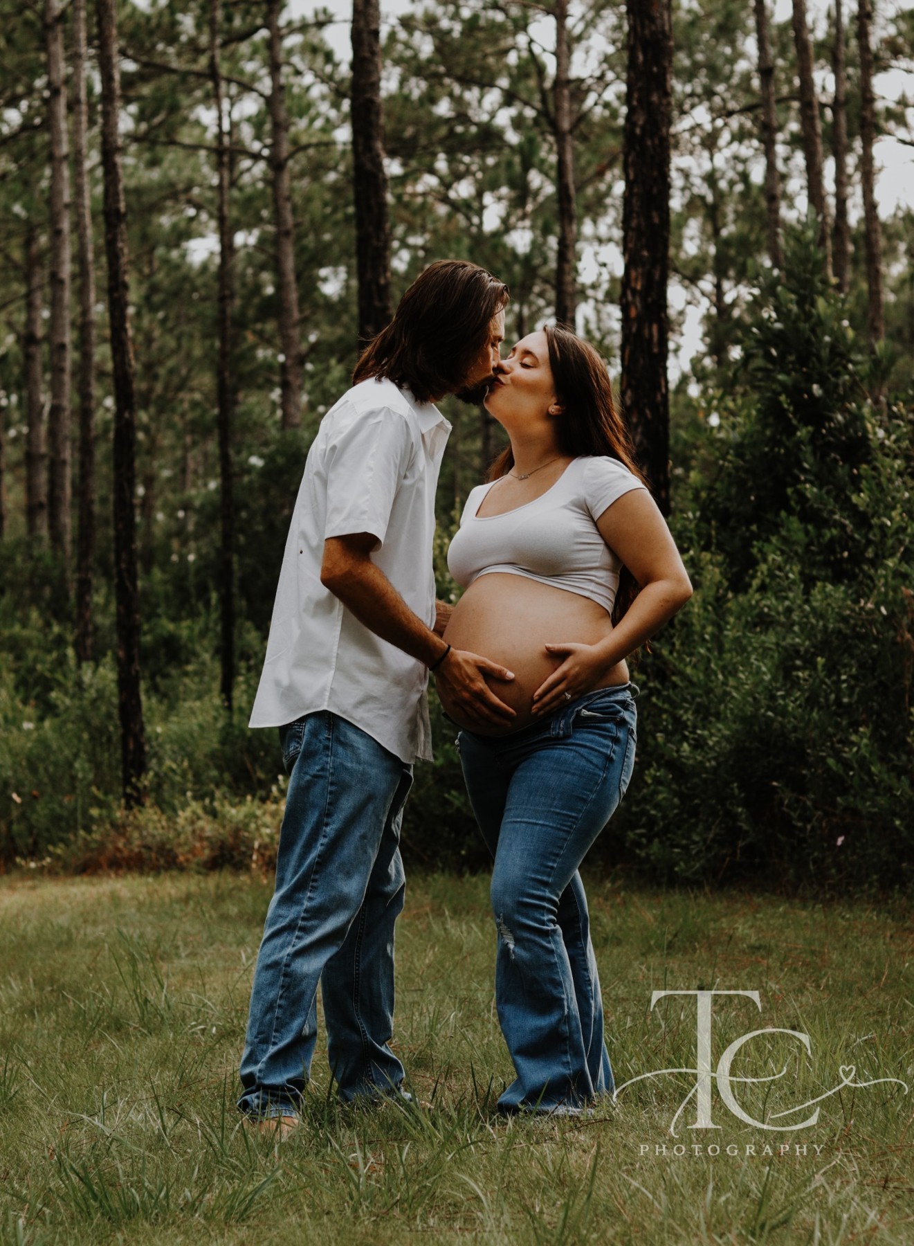 Expectant father kissing the mother beside a woodland path