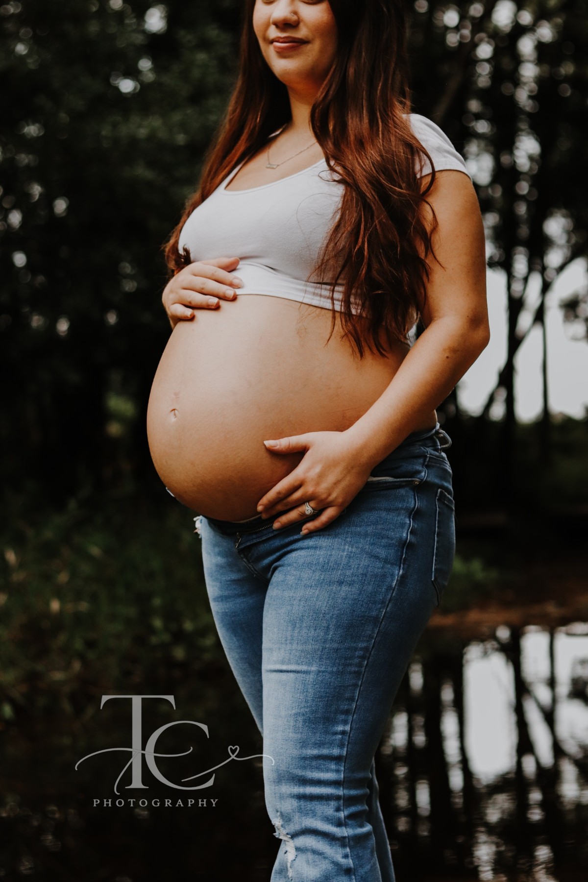 Expectant mother holding her belly beside a pond