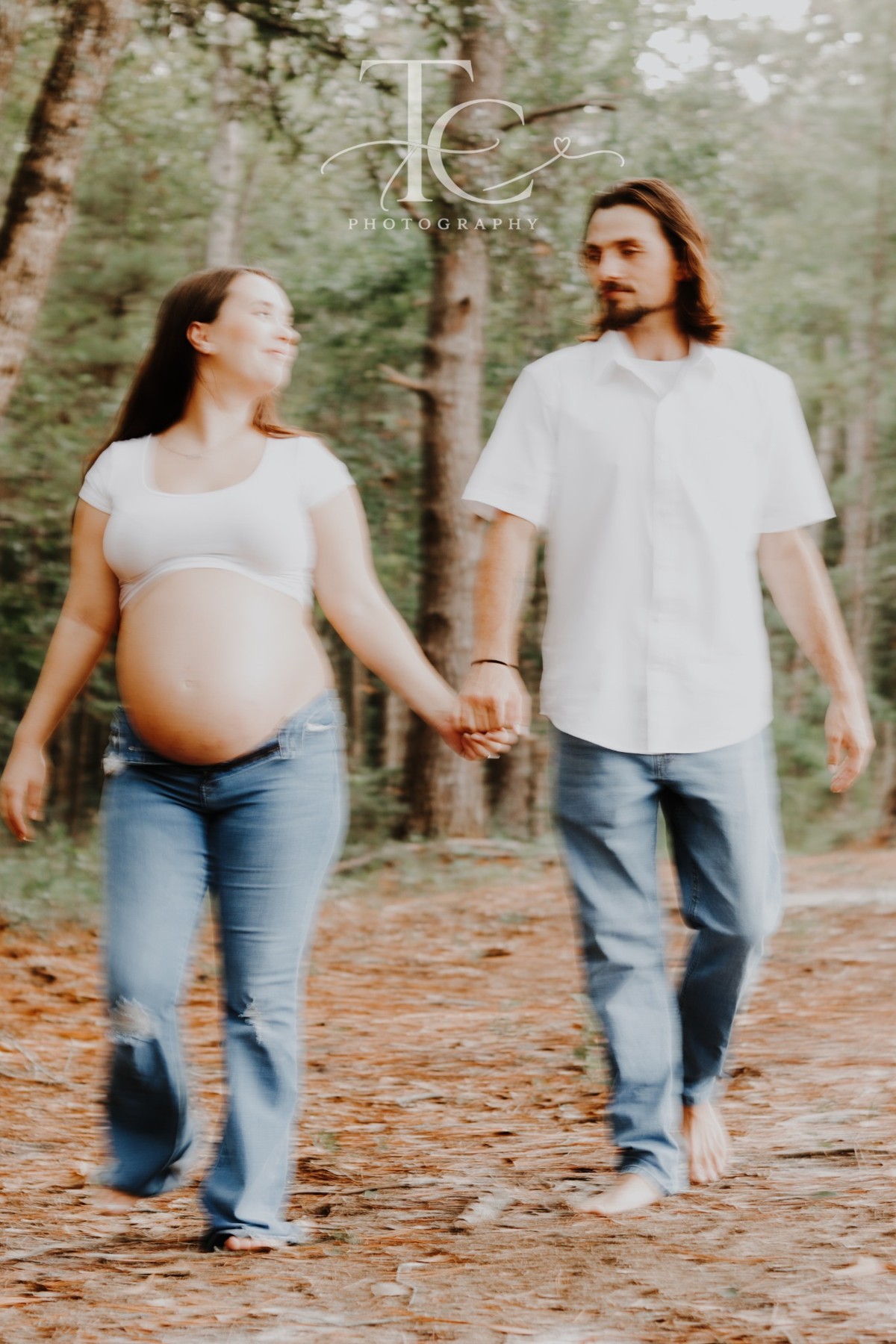 Expectant parents walking hand in hand through the woods