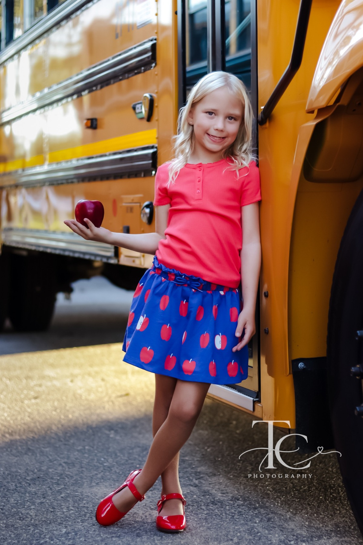 Girl holding a red apple beside a yellow school bus