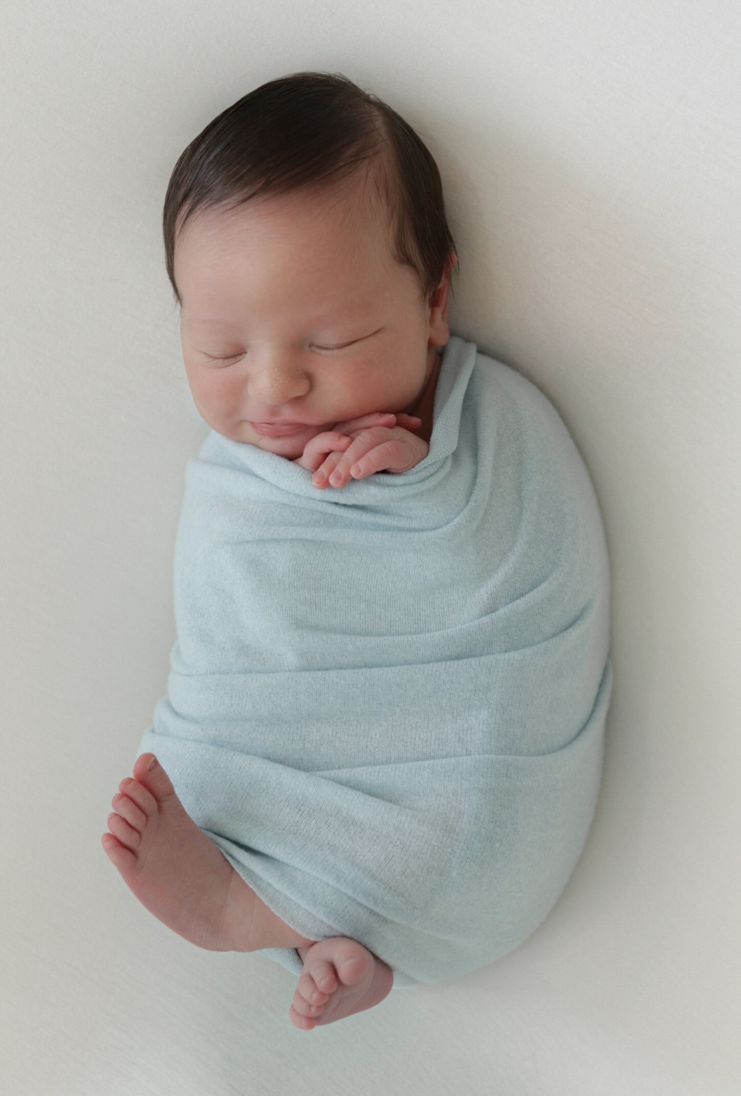 Sleeping newborn wrapped in light blue fabric on a white blanket