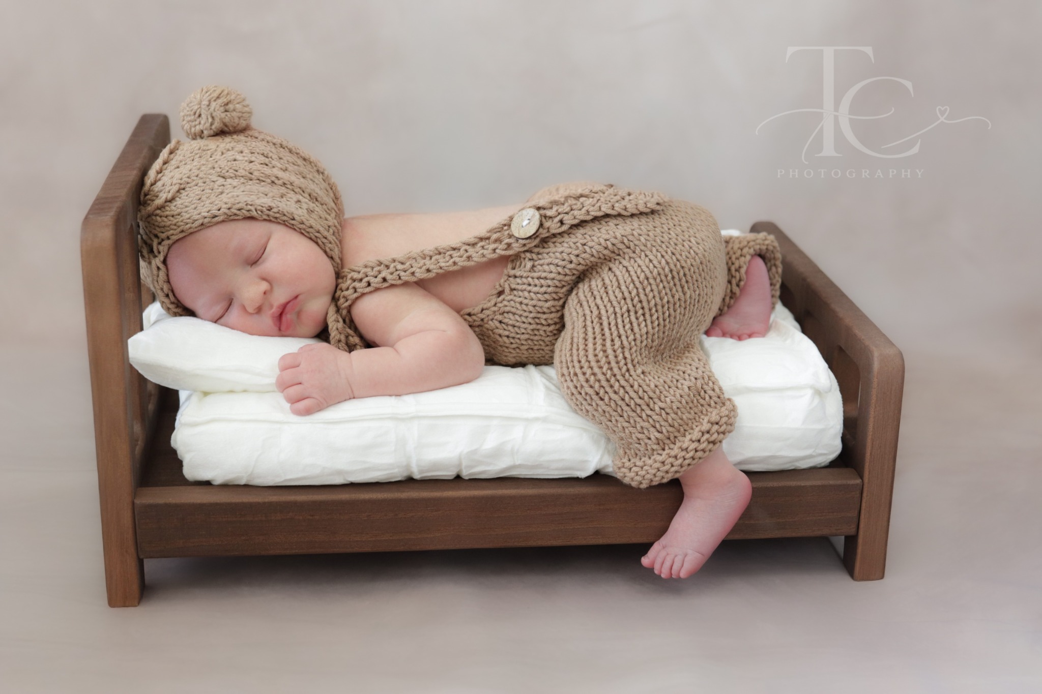 Newborn sleeping in a miniature wooden bed in a brown knit outfit
