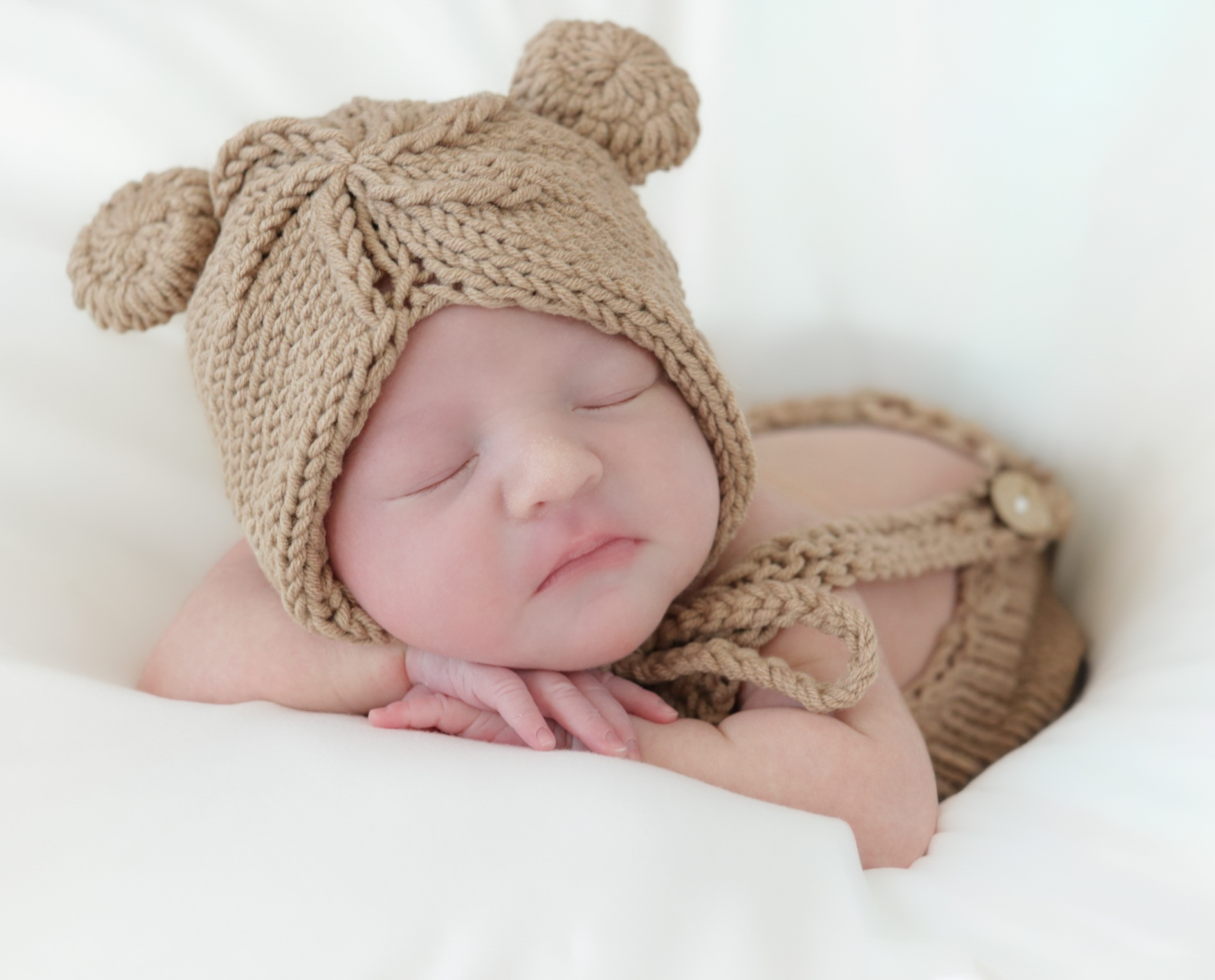 Newborn wearing a brown bear-ear hat with hands beneath the chin